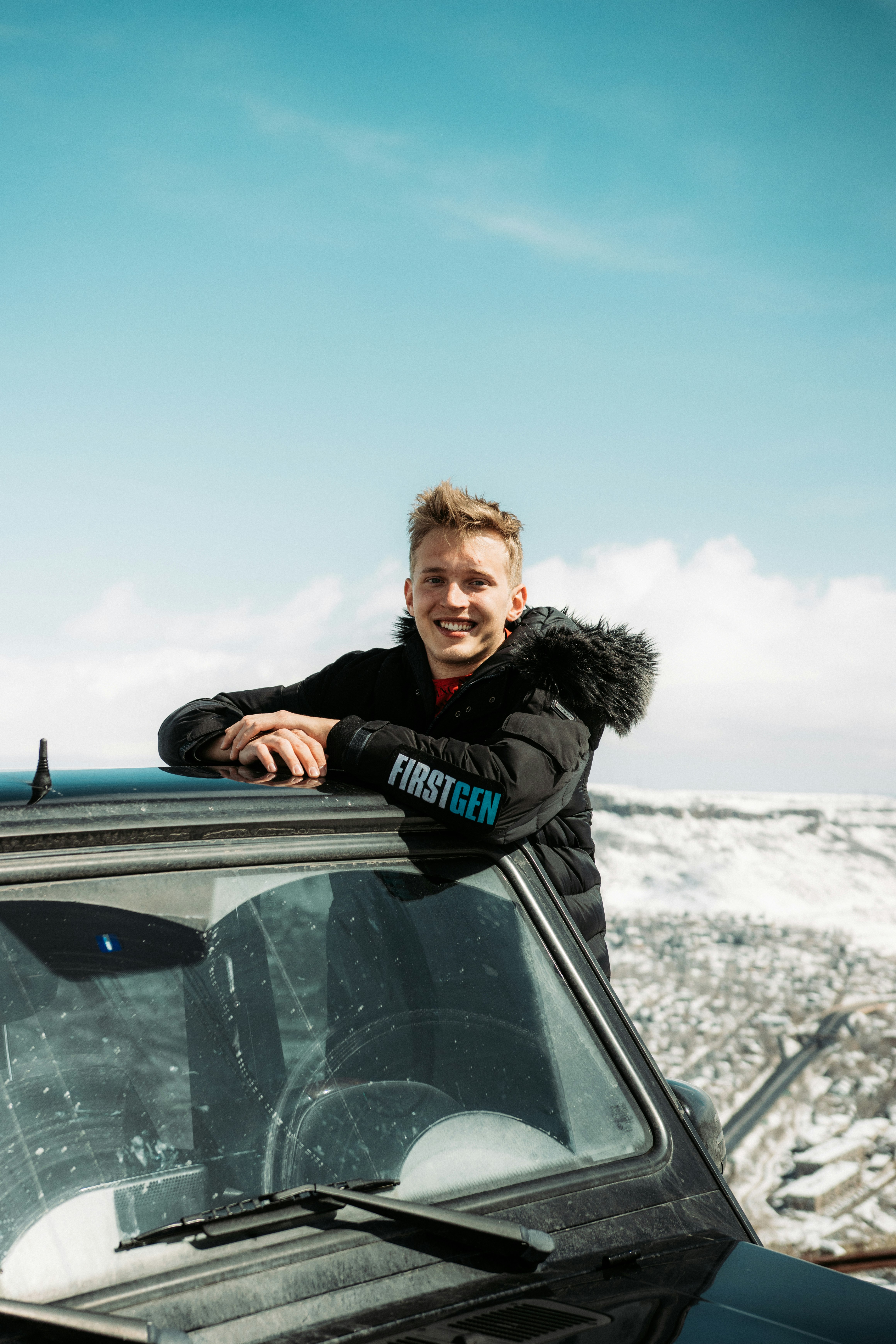 man in black parka jacket leaning on black car during daytime